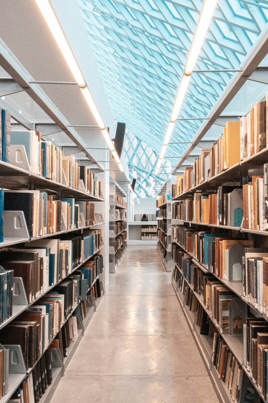 Photograph of books on a bookshelf, looking down an aisle at the library. Photo by Shunya Koide on Unsplash